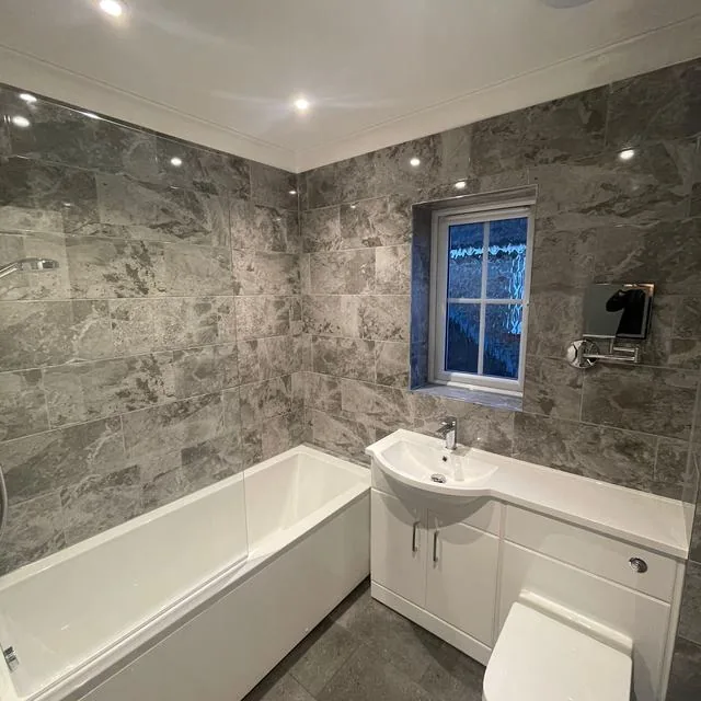 A bathroom with a bath, glass shower screen and tiled surround