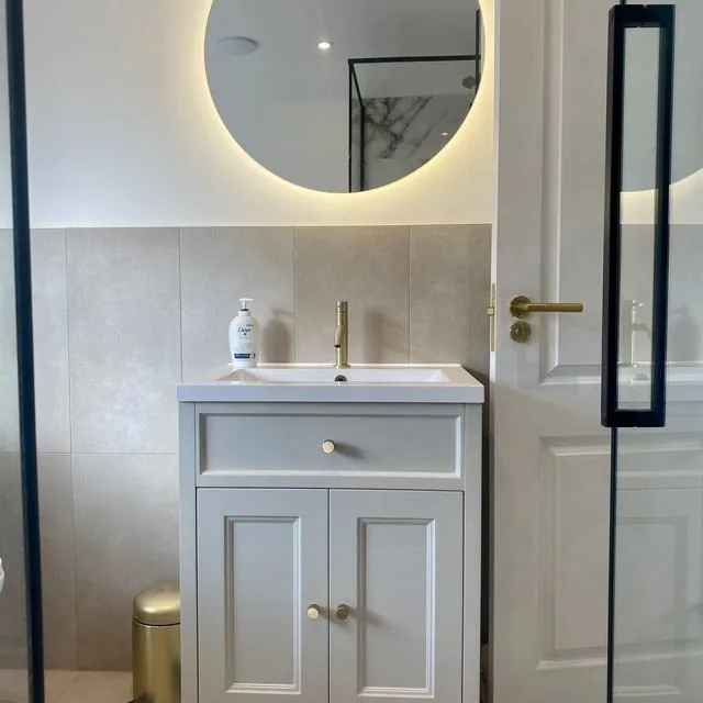 A vanity unit with a brushed brass tap and round mirror