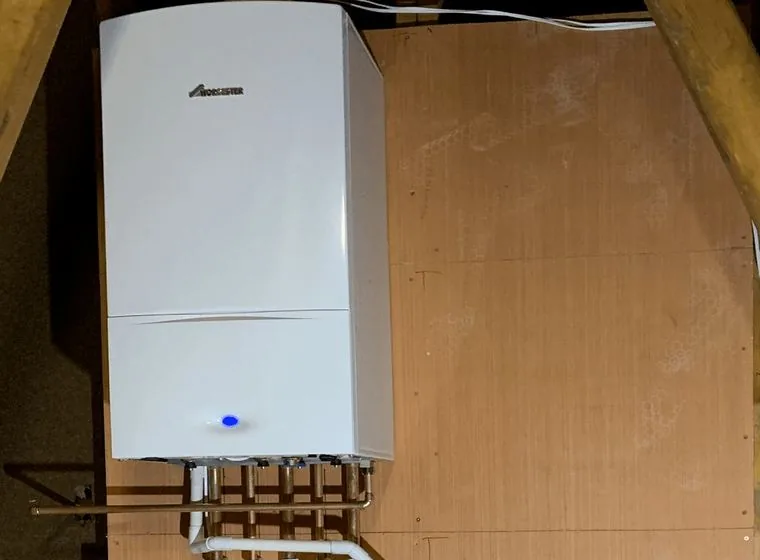 A wall mounted boiler installed in a loft with copper pipework below it