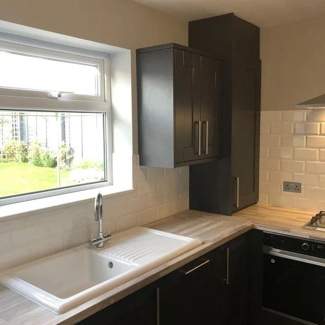 A kitchen with dark cabinets and a window above the worktop