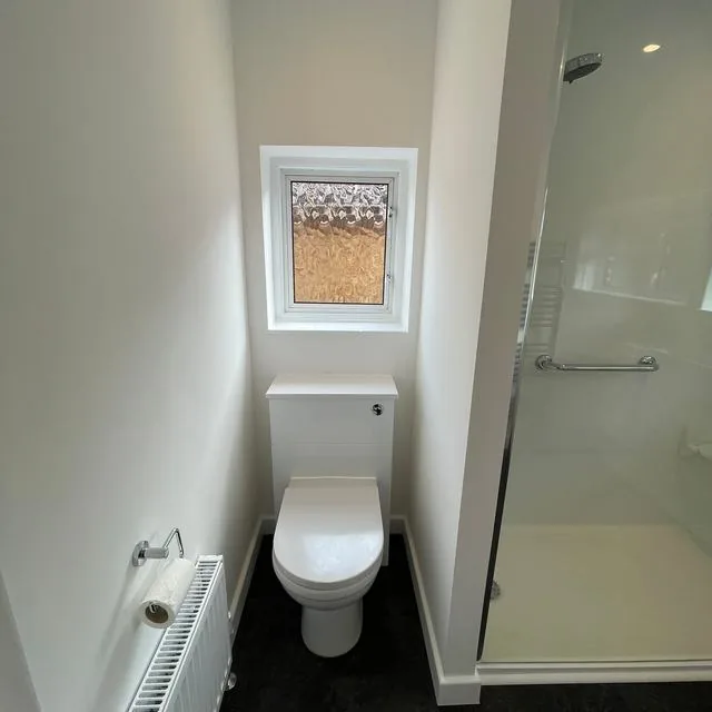 A cloakroom with a toilet, radiator and shower enclosure